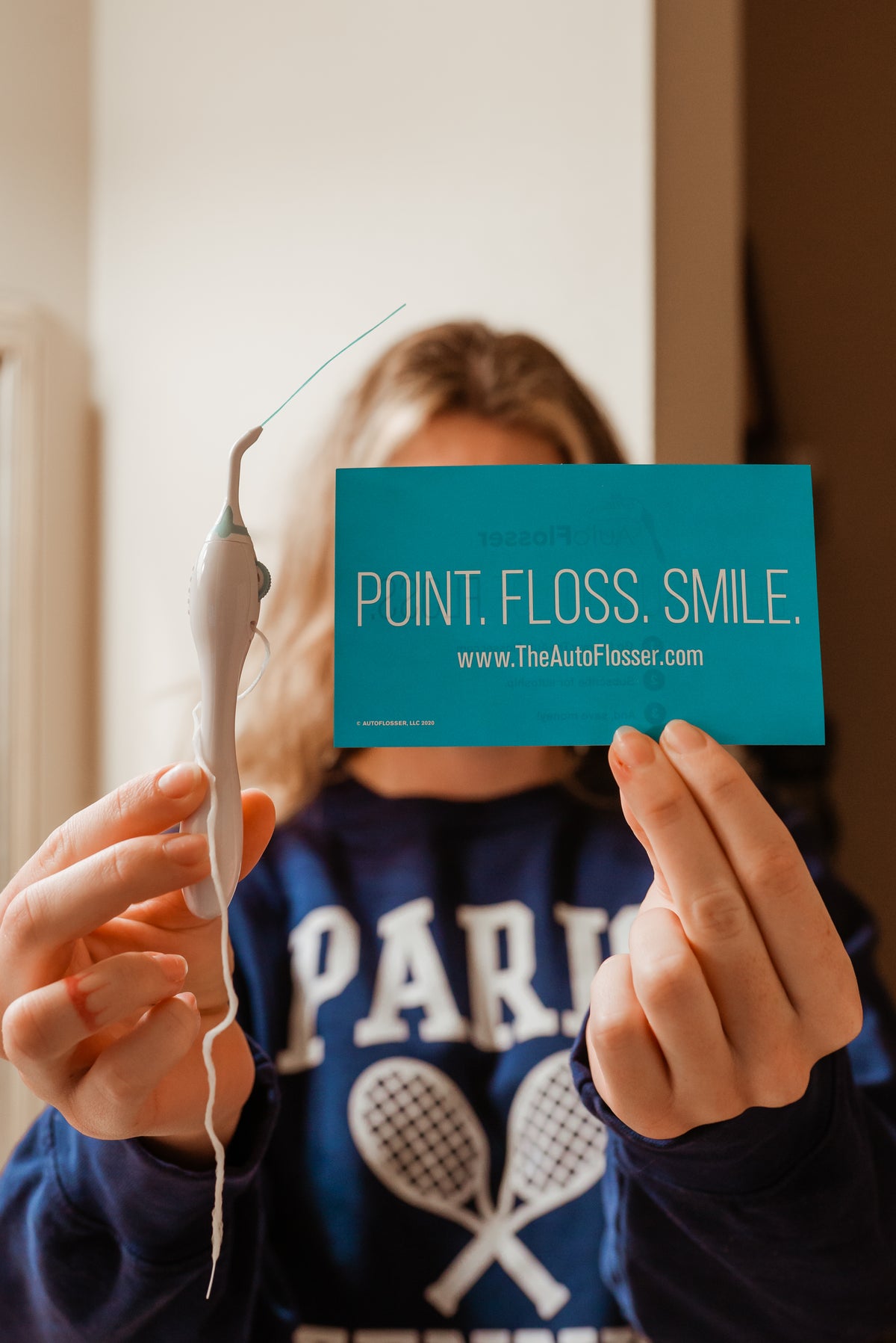 Someone holding up The AutoFlosser and its Point. Floss. Smile. card
